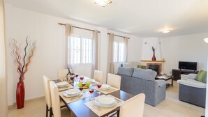 Uma sala de estar moderna com um sofá cinzento, uma mesa de jantar posta com pratos e copos, e uma TV em um móvel.