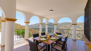 Varanda com mesa posta para o café da manhã, colunas brancas e vista para as colinas.