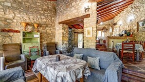 Una habitación rústica con paredes de piedra, un sofá, sillas, una mesa y una zona de comedor con mantel.