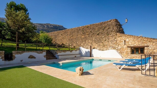 Un edificio de piedra con piscina, mobiliario exterior y una escalera que sube a un nivel superior.