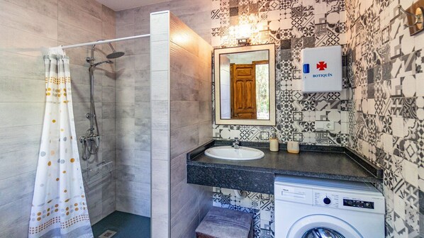 A bathroom with a shower, a sink, a washing machine, and a mirror. - Molino Higueral Villanueva del Trabuco by Ruralidays (Málaga)