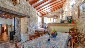 Un comedor de paredes de piedra con una mesa preparada para dos personas, una botella de vino y un florero con flores.