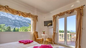A hotel room with two beds, a small table with a chair, a TV, and a balcony with a view of mountains. - Villa Toscana by Interhome (Dénia)