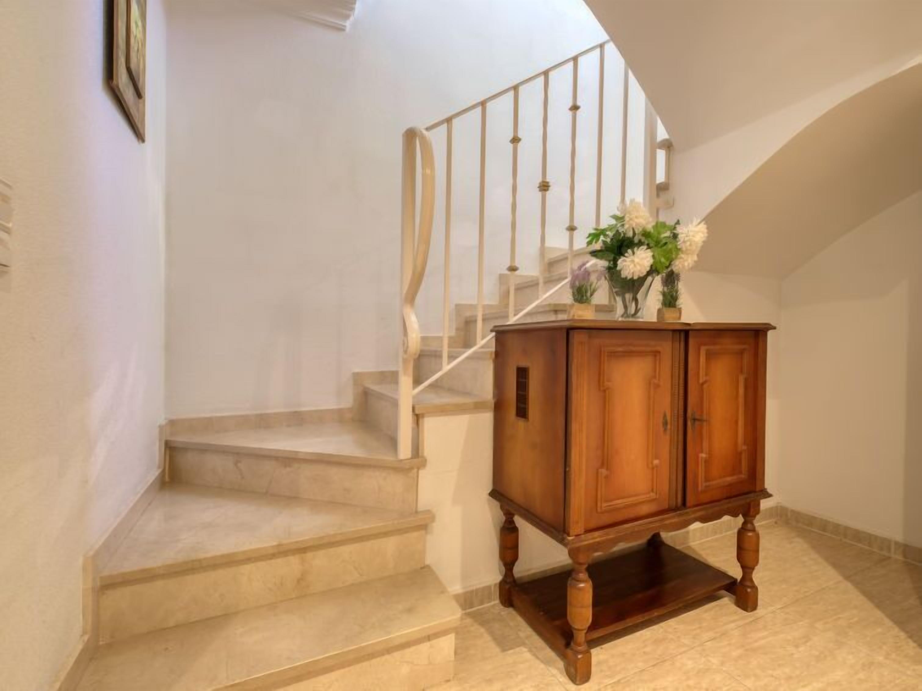 A staircase with a wooden cabinet at the bottom, a white railing, and a framed picture on the wall.