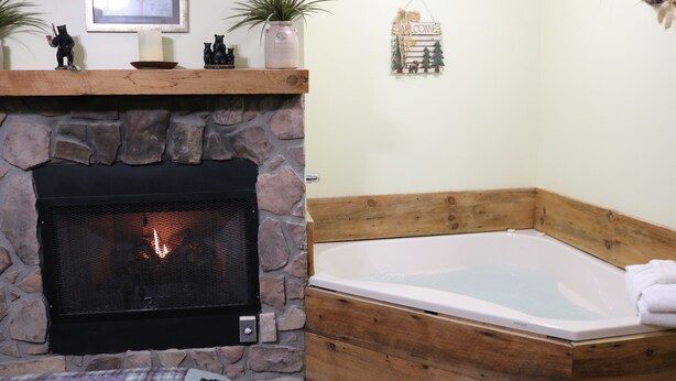 Ein Kamin aus Stein mit Feuer, eine Holzbank und eine Eckbadewanne.