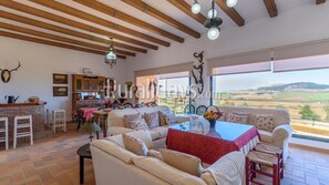 Un'ampia zona giorno con una grande finestra che offre vista sulla campagna, un'accogliente area salotto e un angolo cucina rustico.