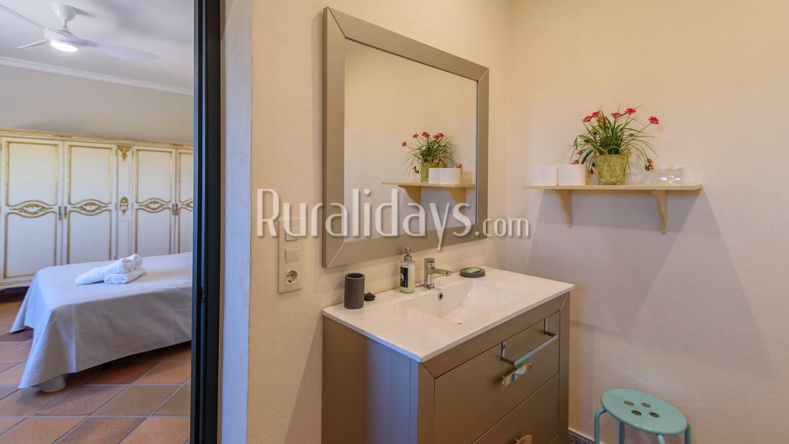 A hotel room with a bed, a bathroom with a sink and mirror, and a shelf with potted plants.