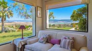 A room with a sofa facing a large window with a view of a landscape. - Cortijo Sierra y Lago Arcos de la Frontera by Ruralidays (Cádiz)