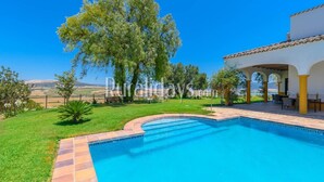 A swimming pool with a curved edge, surrounded by a well-maintained lawn and a patio area with outdoor seating.