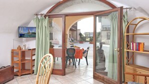 A room with a view of a courtyard, a wooden chair, a table with a green tablecloth, and a bookshelf. - Cosy apartment for 7 guests with A/C, pool, WIFI, TV, patio and pets allowed (Salò)