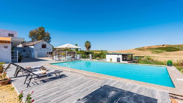Une piscine avec une terrasse en bois, des chaises longues et un petit pavillon.