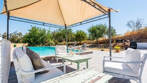 Un espace piscine extérieur comprenant des chaises longues, une table et un auvent.