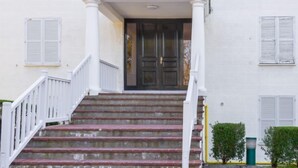 Un bâtiment blanc avec une porte d’entrée, un porche et un escalier menant à l’entrée.