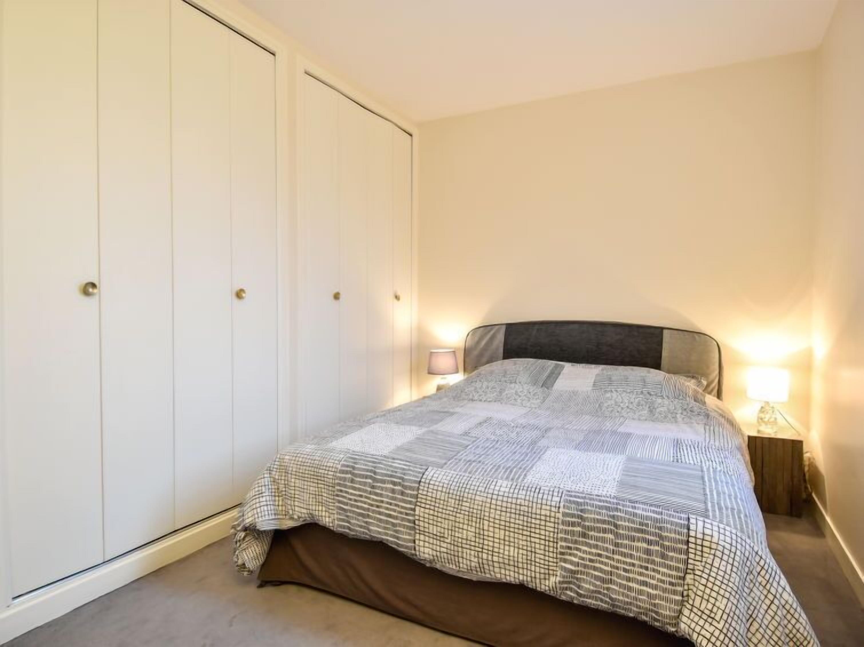 A bedroom with a bed, bedside lamp, and a wardrobe with multiple doors.