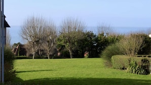 Une pelouse verdoyante, parsemée d’arbres, avec vue sur la mer.