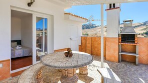 A patio with a round table, a grill, and a view of the countryside.