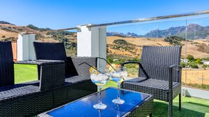 A balcony with wicker furniture, a glass table, and two glasses of a blue beverage with lemon slices. - Casa El Mirador Montecorto by Ruralidays (Málaga)