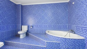 A bathroom with blue mosaic tiles, a toilet, and a freestanding bathtub.