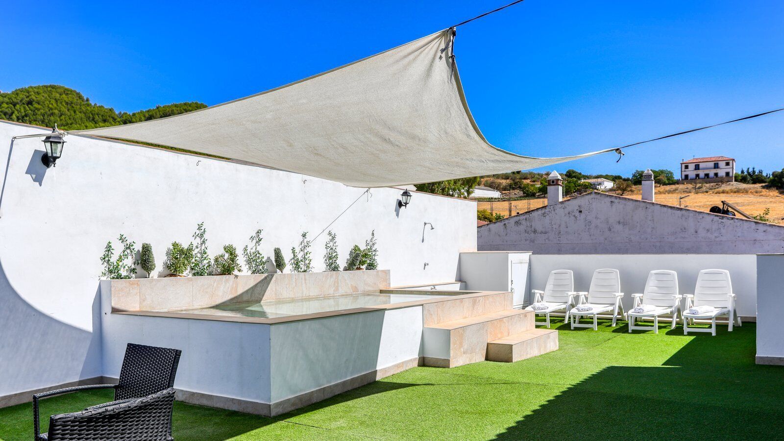 A rooftop terrace with a pool, white lounge chairs, and a pergola providing shade.