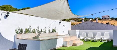 A rooftop terrace with a pool, white lounge chairs, and a pergola providing shade.
