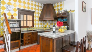 A kitchen with wooden cabinets, a built-in oven, a microwave, and a sink. There is a bottle of Protos wine and a vase with flowers on the island. - Casa El Mirador Montecorto by Ruralidays (Málaga)