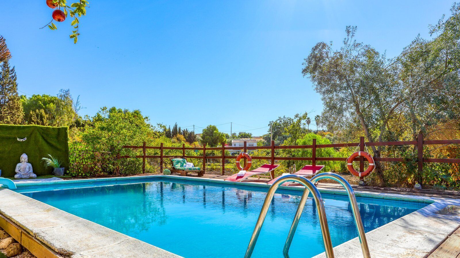 A swimming pool with a wooden deck, lounge chairs, and a Buddha statue.