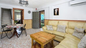A living room with a wooden coffee table, a beige sofa with patterned cushions, a dining table with a checkered tablecloth, and a staircase leading to another room. - Casa Rural La Milla Verde Málaga - Campanillas by Ruralidays (Málaga)