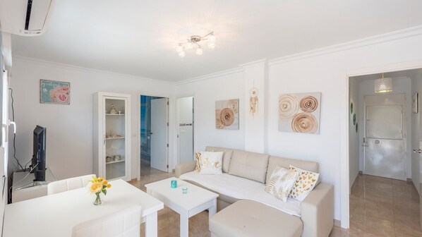 Un salon moderne avec un canapé, une table basse et un téléviseur. On y trouve également des éléments décoratifs muraux et une porte qui donne sur une autre pièce.