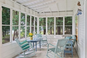 A covered porch with a table and chairs, large windows, and a view of trees. - Waterfront, Dog Friendly Sherwood Point (Sturgeon Bay)