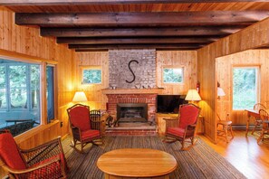 A wooden interior with a stone fireplace, wooden furniture, and large windows. - Waterfront, Dog Friendly Sherwood Point (Sturgeon Bay)