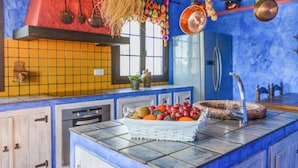 Une cuisine avec un mur recouvert de carreaux, un panier de fruits posé sur le comptoir et un porte-ustensiles suspendu.