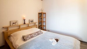 A bedroom with a wooden headboard, a bed with a striped bedspread, a pillow, and slippers on the bed. There is a shelf with framed pictures and a candle on it. - Le Prariond (Val Claret) by Interhome (Tignes)