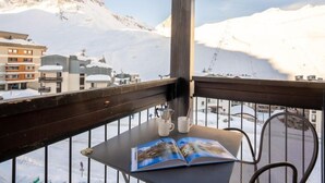 A balcony with a view of snow-covered mountains and a book on a table. - Le Prariond (Val Claret) by Interhome (Tignes)