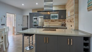 Une cuisine moderne avec des meubles gris, une hotte en acier inoxydable et un îlot central doté de tabourets de bar.
