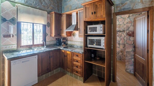 A kitchen with wooden cabinets, a dishwasher, a microwave, and a coffee maker. - Villa Rústica de Conil Conil de la Frontera by Ruralidays (Cádiz)