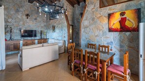 A stone-walled room with a dining table, chairs, a sofa, and a TV.