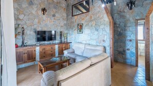A stone-walled living room with a sofa, wooden cabinets, a TV, and a fireplace.