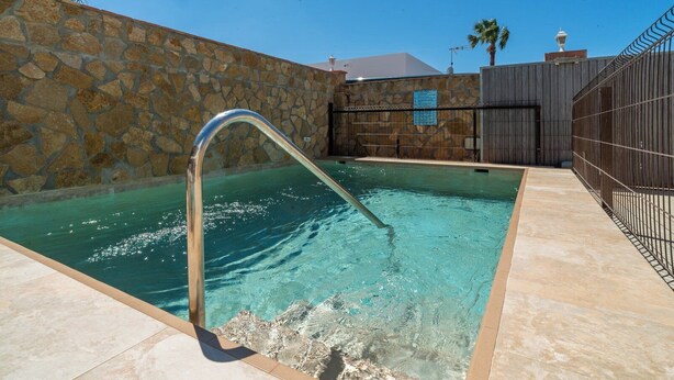 A swimming pool with a stone wall and a metal fence.