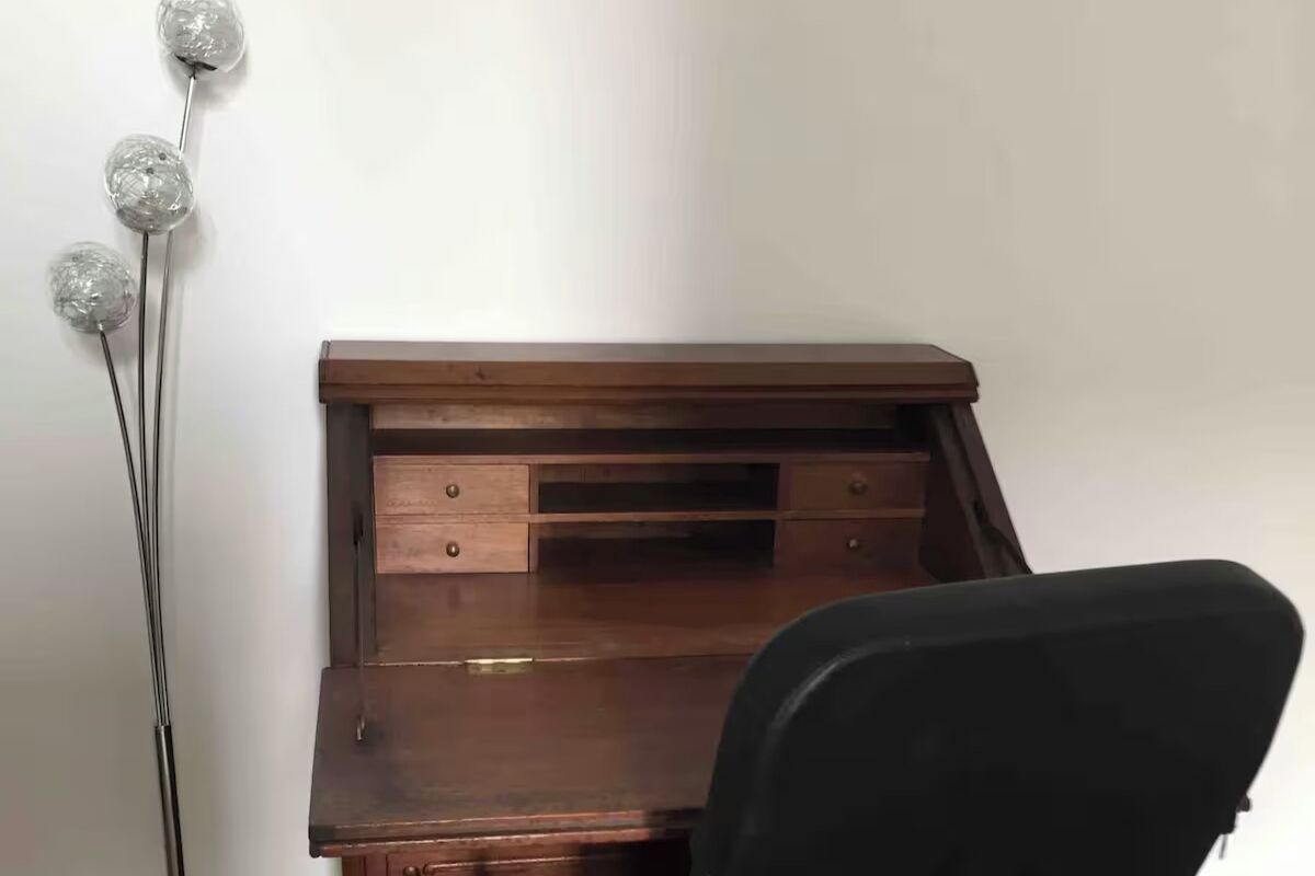 A wooden desk with drawers and a black chair in front.