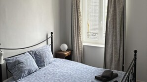 A bedroom with a bed, a bedside table with a lamp, and a window with curtains. - 2 Bed-Roof Terrace-Town Centre-Pets (Montmorillon)