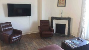 A living room with a flat-screen TV mounted on the wall, a fireplace, two leather armchairs, and a coffee table with magazines. - 2 Bed-Roof Terrace-Town Centre-Pets (Montmorillon)