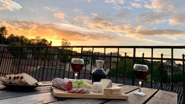 A wooden table with a cheese board, grapes, and wine glasses on a balcony with a sunset view. - 2 Bed-Roof Terrace-Town Centre-Pets (Montmorillon)