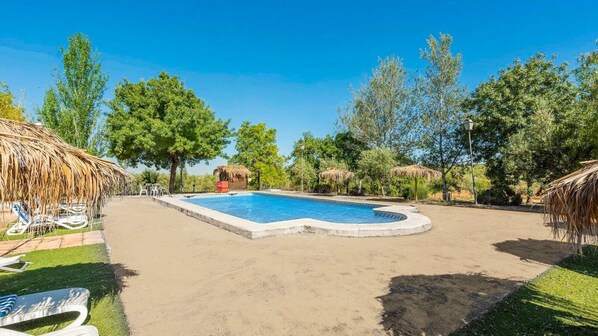 A swimming pool with a thatched roof structure, surrounded by trees and a clear sky. - Cortijo Carrillo Antequera by Ruralidays (Málaga)