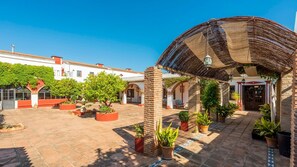 A courtyard with a covered seating area, potted plants, and a building with a tiled roof. - Cortijo Carrillo Antequera by Ruralidays (Málaga)