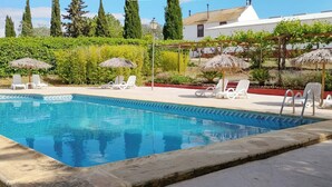 A swimming pool with lounge chairs and umbrellas, surrounded by greenery and a building in the background. - Cortijo Carrillo Antequera by Ruralidays (Málaga)