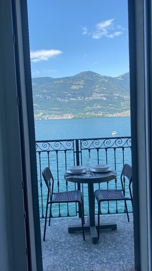 A balcony with a table and chairs, overlooking a body of water and a mountainous landscape.