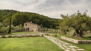 Un edificio de piedra con techo de tejas, rodeado de un jardín bien cuidado con un camino de piedra que lleva a la entrada.