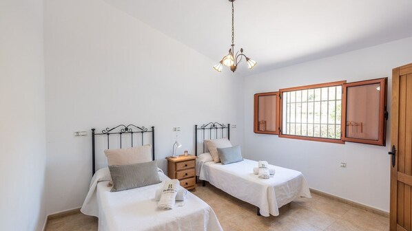 A bedroom with two single beds, a nightstand, a lamp, and a window with wooden shutters. - Villa Virginia Arenas by Ruralidays (Málaga)