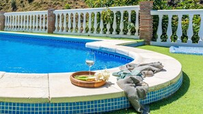 Zwembad met een witte balustrade, een glas witte wijn en een bord met eten en servetten op een zonnig terras.