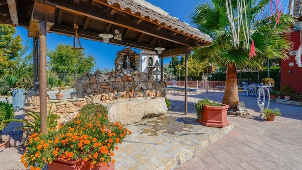 A stone structure with a statue, surrounded by potted plants and a tiled patio area.